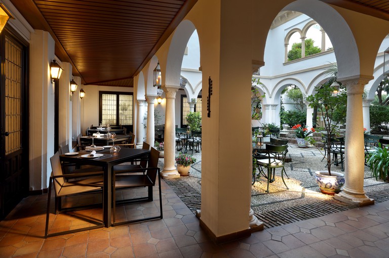 Tables and chairs for dining in the courtyard of Eurostars Conquistador in Córdoba, with rounded arches and potted plants