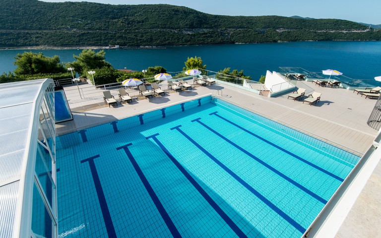 The outdoor pool and sunbeds at Grand Hotel Neum, with the blue sea and forested cliffs in the distance