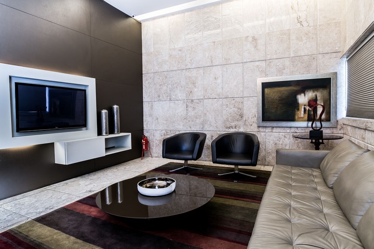 A living room at Savassi Hotel with a grey leather sofa opposite a wall-mounted TV