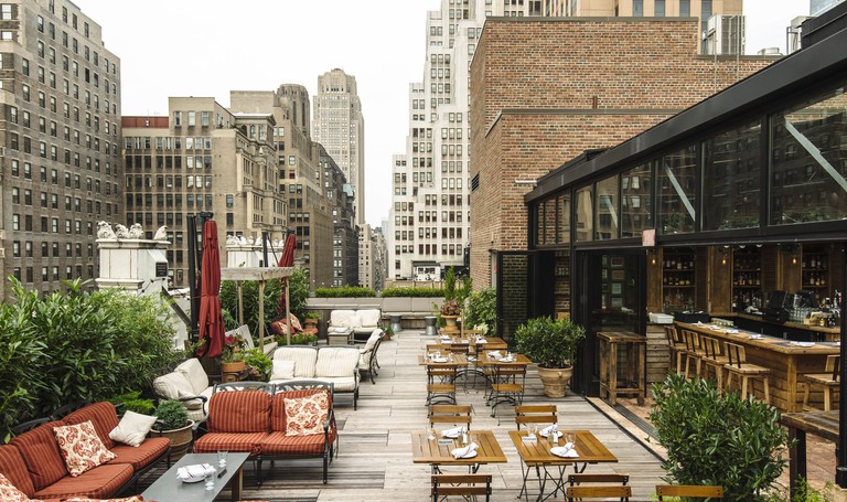 Stylish rooftop dining and lounge seating with views of nearby buildings at Refinery Hotel in New York City