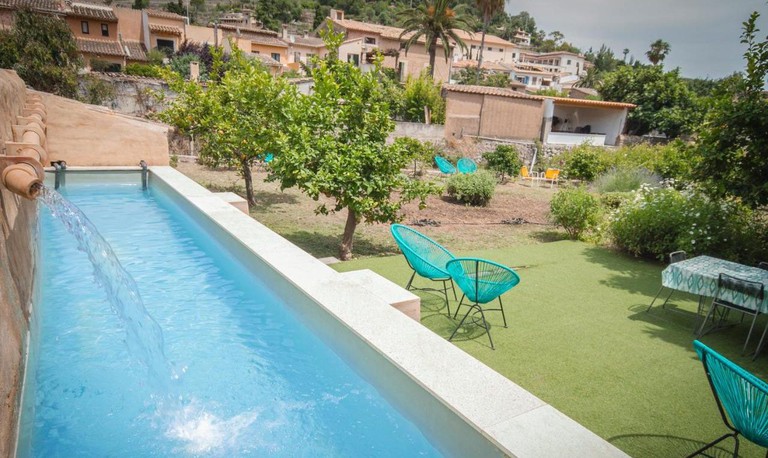 Outdoor pool area at Hostel Sa Fita Backpackers features manicured lawns, bright blue chairs and orange trees