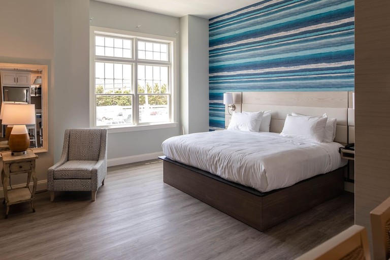 A double bed against a striped blue accent wall in a simple room with gray hardwood floors and a gray chair at Hotel LBI