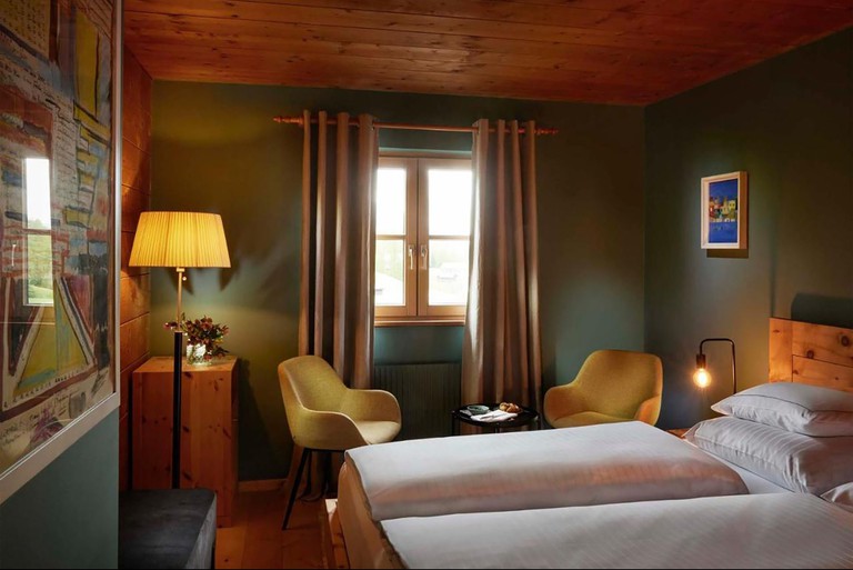 A bed with two duvets, two yellow armchairs and a wood plank ceiling in a cosy hotel room at Hotel Gasthof Hirschen Schwarzenberg