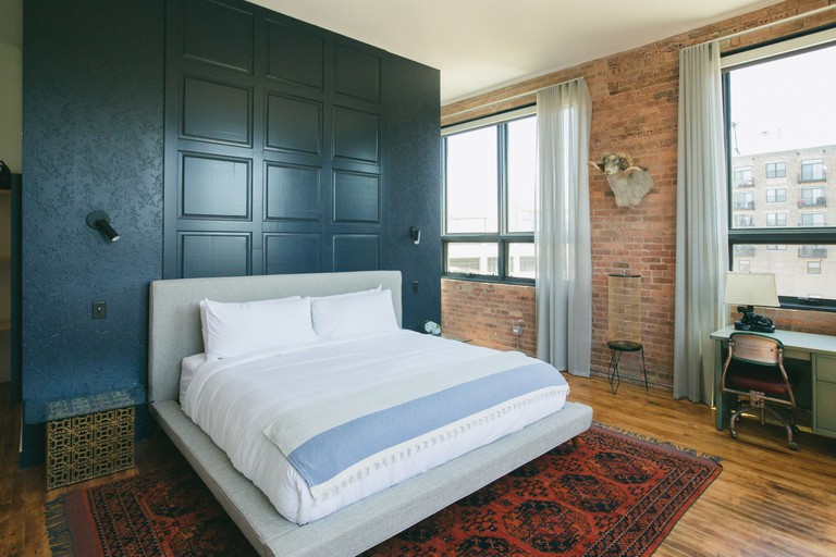 A bedroom at the Publishing House Bed and Breakfast, with a wooden floor, turquoise wall, a bed and exposed brick wall