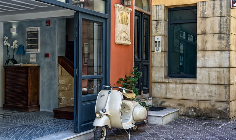 Exterior of Vranas Ambiance Hotel with a parked-up Vespa next to the door and a casual lobby to the left.