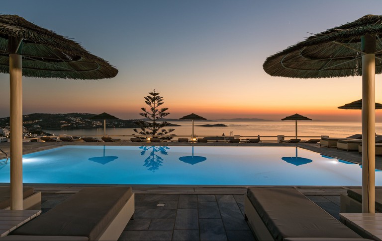 Outdoor swimming pool at Hotel Alkyon with wicker parasols and a view of the sea at sunset