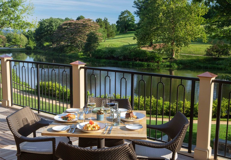 A table on a balcony at Boar’s Head Resort, topped with meals and drinks and with water and garden views