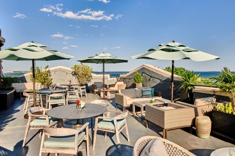 Lounge area with tables, wooden chairs and light turquoise umbrellas with panoramic views of the harbor at Harborview Inn