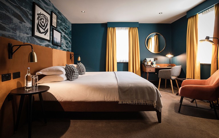 Stylish, cosy guest room at Hotel du Vin Stratford-Upon-Avon with dark blue walls, mid-century furniture and plush coffee-hued carpet