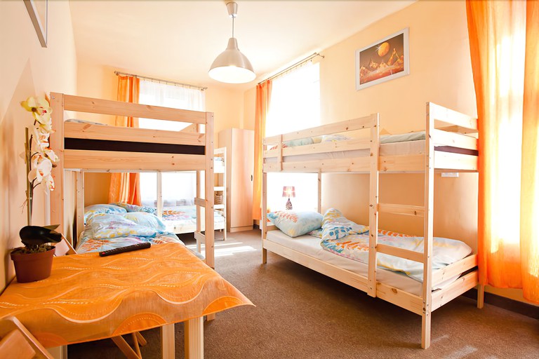 Wood bunkbeds, a table and orange drapes in a hostel dorm room at Moon Hostel