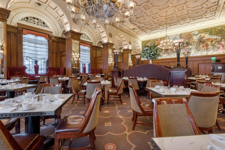 A grand dining room at Omni William Penn Hotel featuring dark-wood chairs and industrial tables, plus a mural on the wall