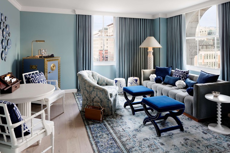 A stylish and quirky room at the Riggs Washington DC, with a cushioned sofa, two footstools, an armchair and a small table with two cushioned chairs.