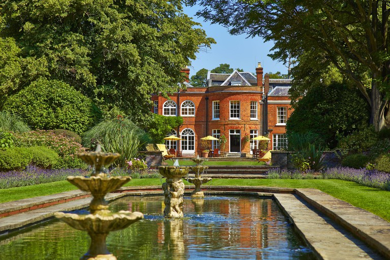 Outdoor gardens of the Royal Berkshire Hotel, with a small lake with water fountains, lavender bushes and tall trees