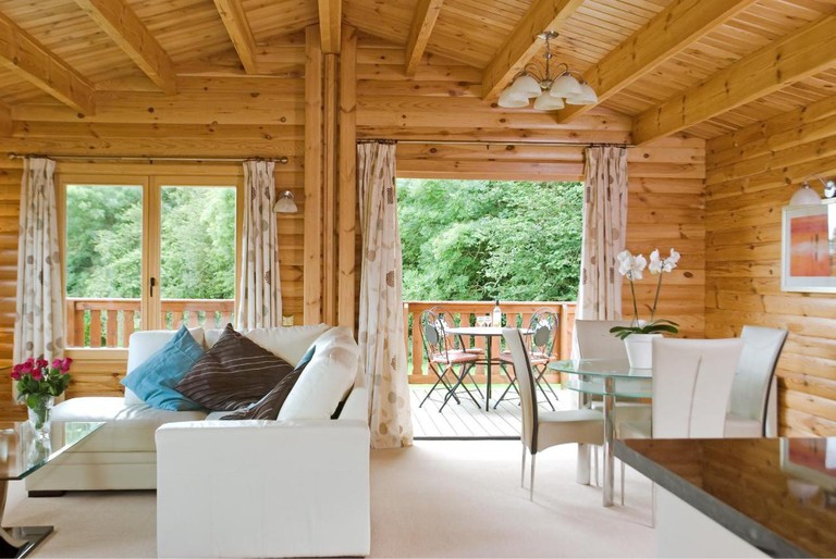 Living and dining area of Scandinavian-style log cabin with large deck overlooking greenery at South Winchester Lodges