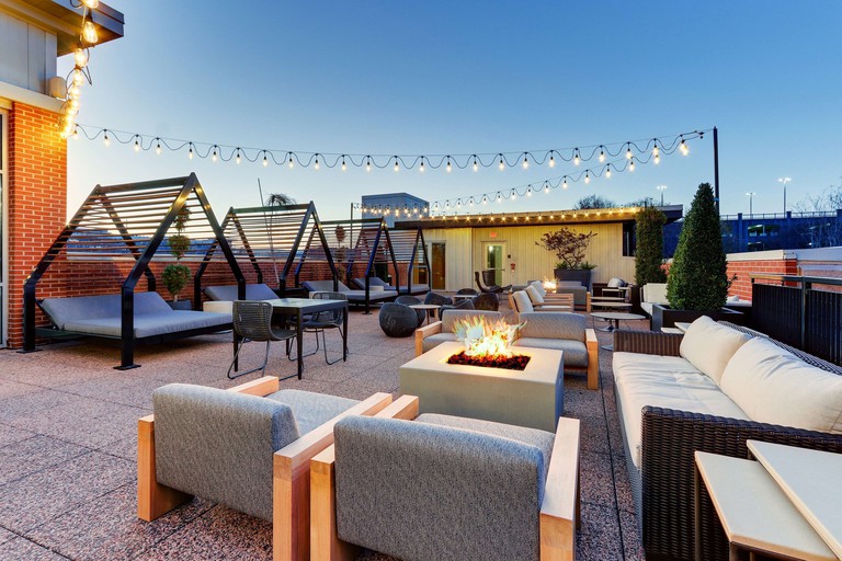 Rooftop terrace at the Chattanoogan Hotel, featuring outdoor tables and chairs arranged around fire pits as well as large daybeds, all under hanging fairy lights