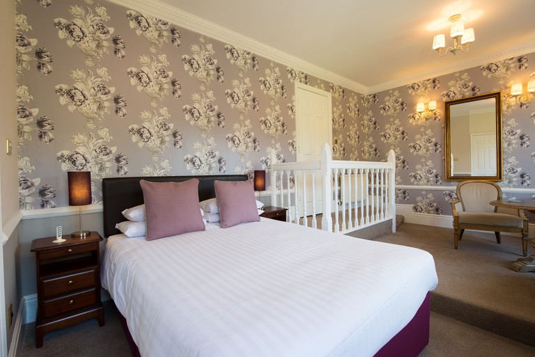 A bedroom with a cushioned bed and mirror at Woodlands Lodge Hotel