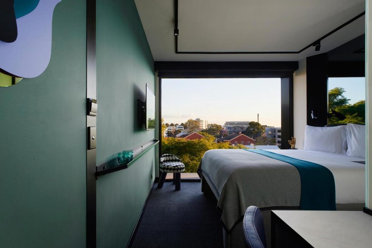 Snug modern bedroom with large bed, olive green walls, charcoal carpeting and floor-to-ceiling window