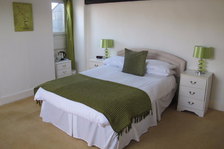 A comfortable carpeted bedroom at Fairlawn House in Salisbury featuring a bed with a green throw and green lamps