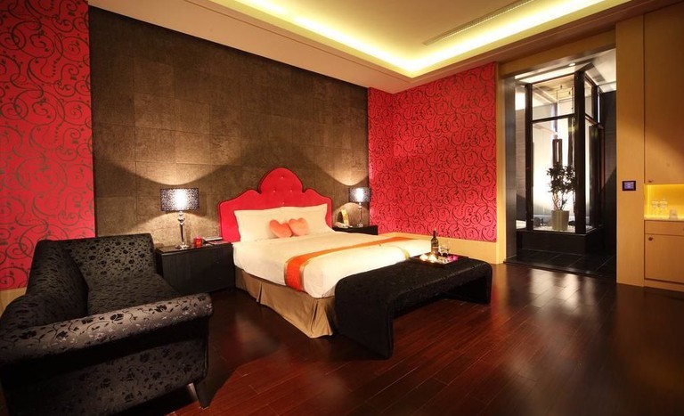 Sumptuous bedroom with red silk wallpaper, dark wood floors large bed and black satin fabric sofa