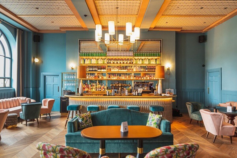 A trendy bar at The Clarence Hotel with comfy seating and a brightly coloured decor