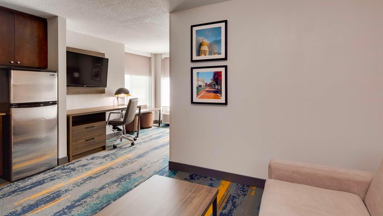 A room at Best Western Plus Augusta North Inn & Suites, containing a sofa, fridge and a wall-mounted TV above an office chair and desk