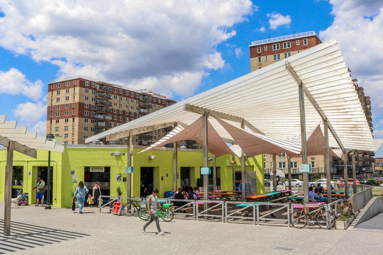 The exterior view of Rippers avocado-colored building and shade sails on the Rockaway beachfront boardwalk