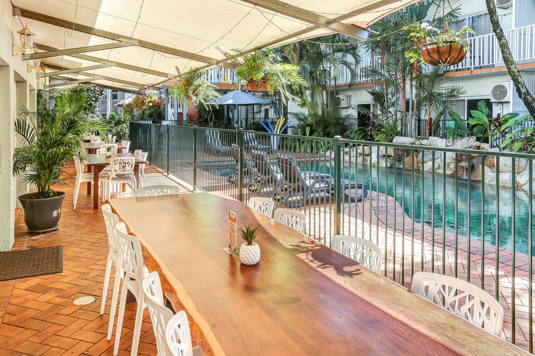 Long wooden tables under an awning facing the pool at Coral Tree Inn