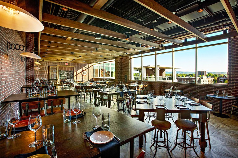 A red-brick dining area at Embassy Suites by Hilton Greenville Downtown Riverplace overlooking countryside, with numerous wooden tables, chairs and stools