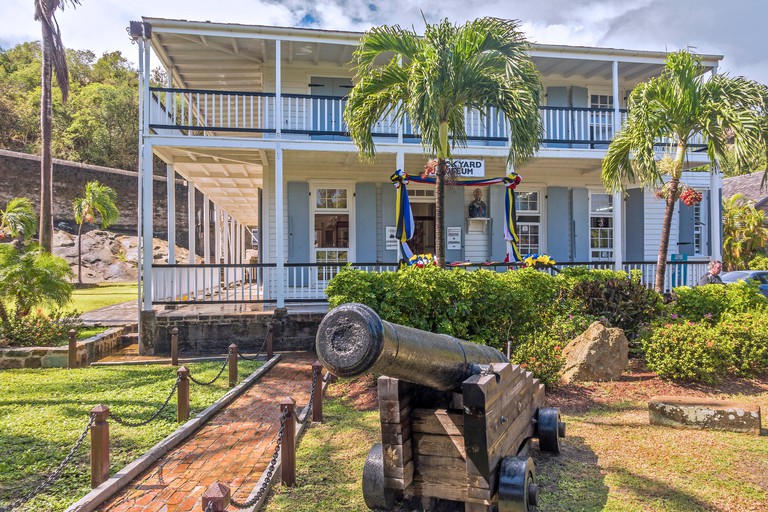 An old canon sits in front of the blue-painted Dockyard Museum in Nelson's Dockyard