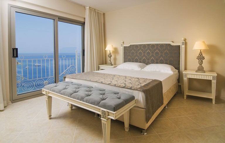 Upscale bedroom with large bed, neutral-tone traditional furnishings and sliding doors to railing with sea view