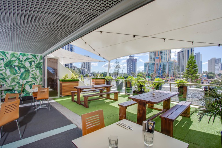Exterior restaurant area with wood tables and benches and shade coverings with view of city