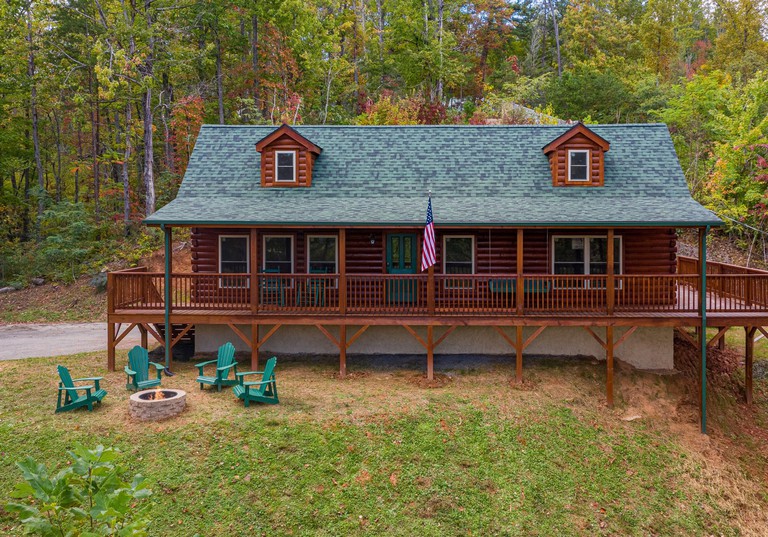 The exterior of Smoky Retreat log cabin, with four chairs surrounding a fire pit in the adjoining woodland