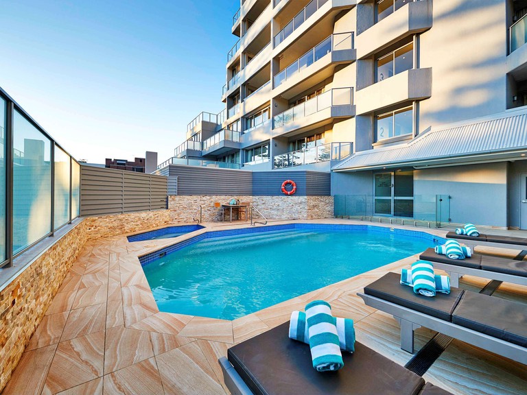 View of angular swimming pool and marble tiles with sun loungers at The Sebel Sydney Manly Beach