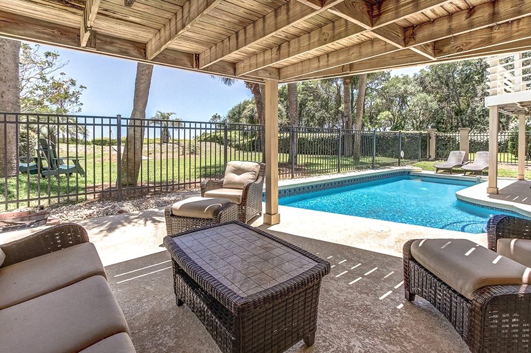 A covered outdoor lounging area next to the pool at the five-bedroom, five-bath Cassina Palms condo