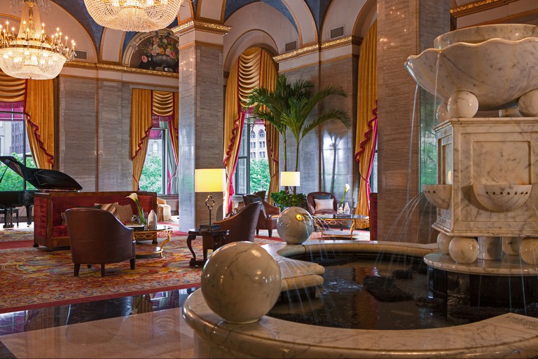 A large, luxury communal area at Renaissance Cleveland Hotel, with marble flooring, a marble fountain, a piano and grand wooden furniture