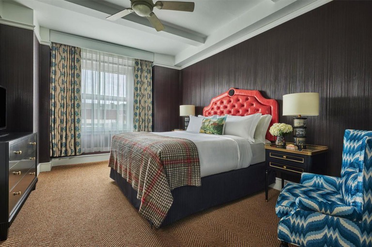 A bedroom at Graduate Providence with dark brown walls, a brown carpet, a double bed with a red headboard and a blue-and-white armchair