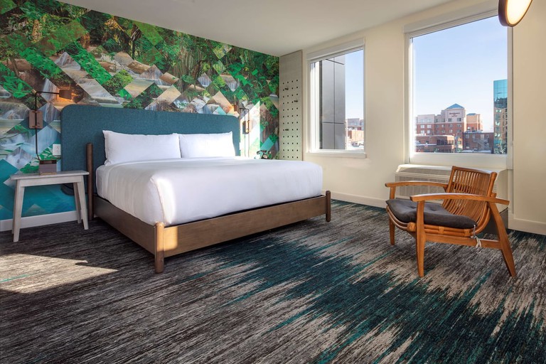 A characterful guest room the Canvas Moncton, Tapestry Collection by Hilton, with a bold feature wall, a king-size bed, a lounge chair and large windows