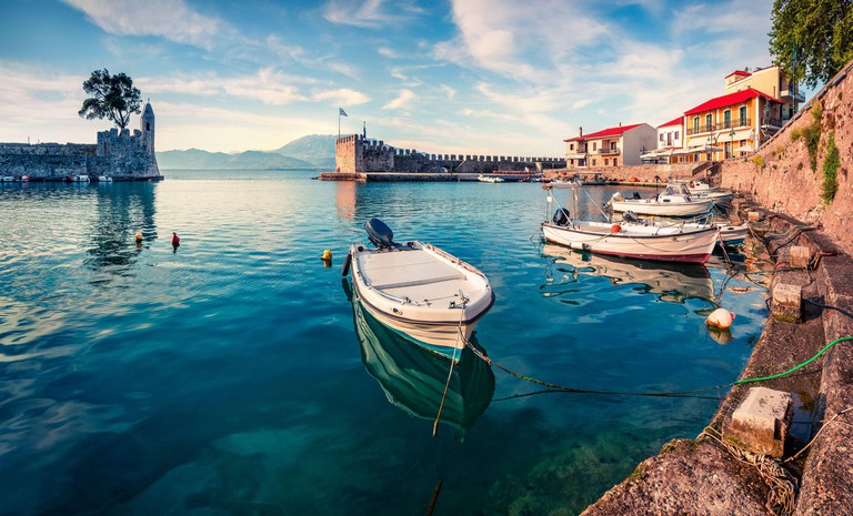 Crescent-shaped Nafpaktos Marina has ancient stone moorings and an attractive crenelated sea wall, with mountains visible in the distance behind it.