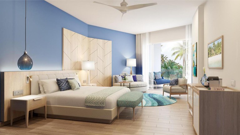 A beachy bedroom at Azul Beach Resort Cap Cana with blue walls, wooden floors and views out to palm trees.