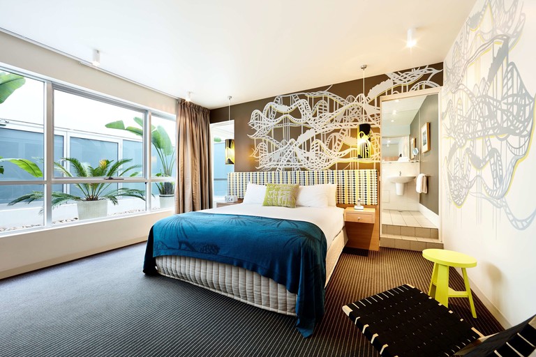 A spacious suite with one bed, murals, bold colours and views of potted plants outside the large windows at the Rydges St Kilda Melbourne