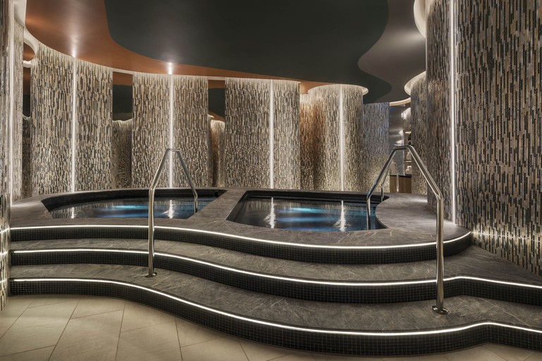 Two mineral pools set in black stone with patterned stone walls in W Brisbane's Away Spa