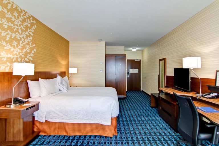 Large king room with wood furnishings, bright blue patterned carpeting and patterned feature wall at Fairfield Inn and Suites by Marriott Kamloops