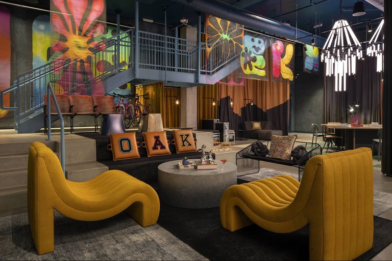 Boldly decorated seating area at Moxy Oakland Downtown with large yellow chairs and hanging silk screens