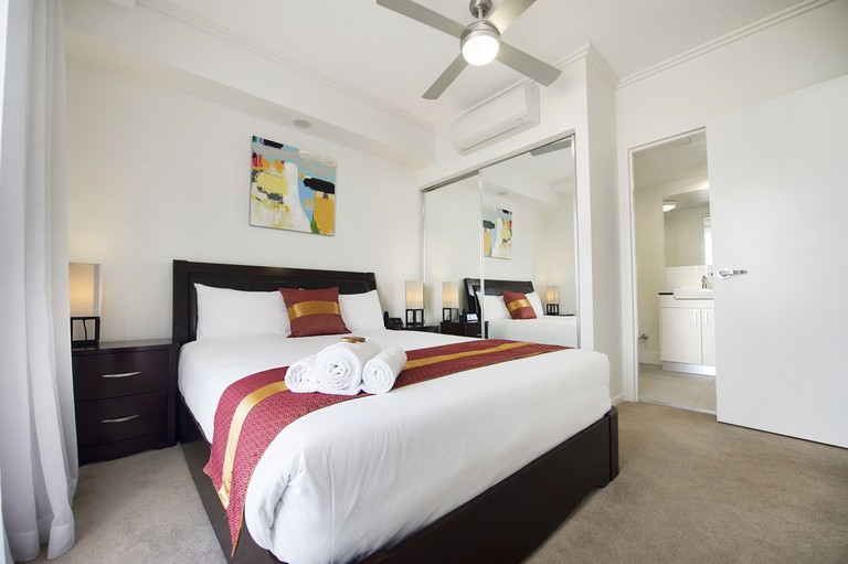 Clean, white room at the Gladstone Central Plaza, with a dark-wood double bed and a white en-suite bathroom.