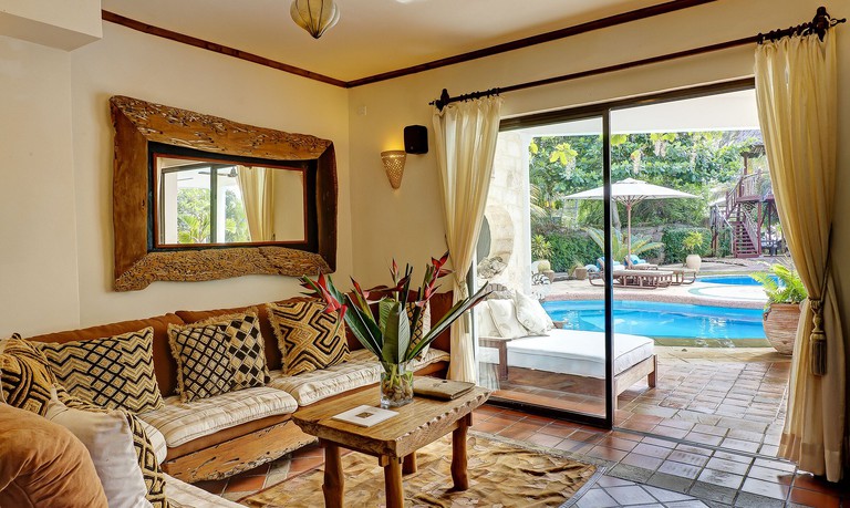 A living area containing a corner sofa at Elewana AfroChic Diani Beach, with a glass door opening towards an outdoor pool