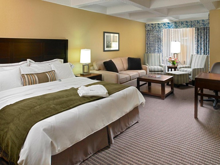 A warm, homey guest room with a king-size bed, a sofa bed and two striped armchairs at the Radisson Hotel Edmonton South