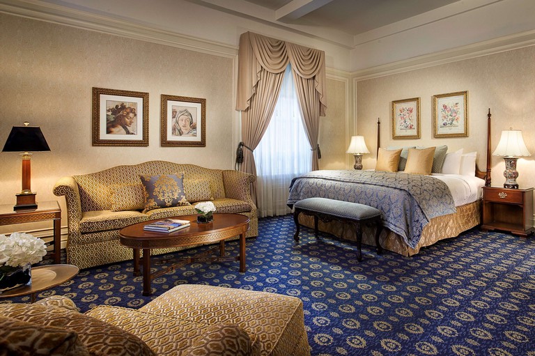 A blue-and-gold suite at Amway Grand Plaza, Curio Collection by Hilton, containing a sofa, soft seat and double bed