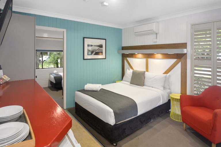 A guestroom at Pleasant Way River Lodge has a bed with a timber headboard and boldly coloured walls and furniture