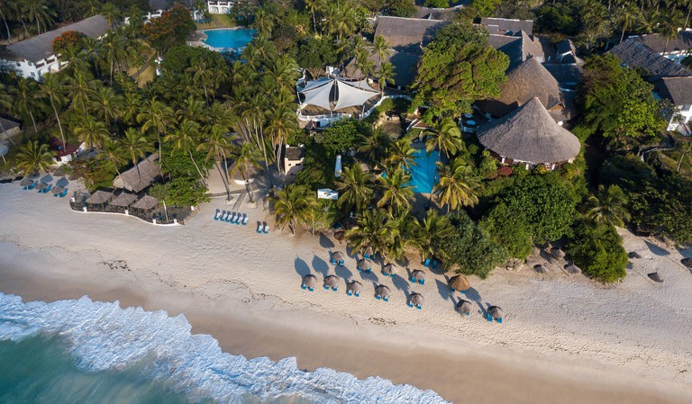 An aerial view of the sand and lapping ocean ahead of the trees surrounding Leisure Lodge Beach & Golf Resort