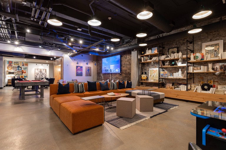 A vibrant lobby area at the Moxy Nashville Downtown, with orange sofas, games and a TV